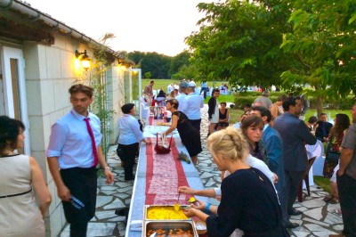 Chambre mansardée avec lit double, poutre apparente, télévision murale, commode, chaise et lampe de chevet.