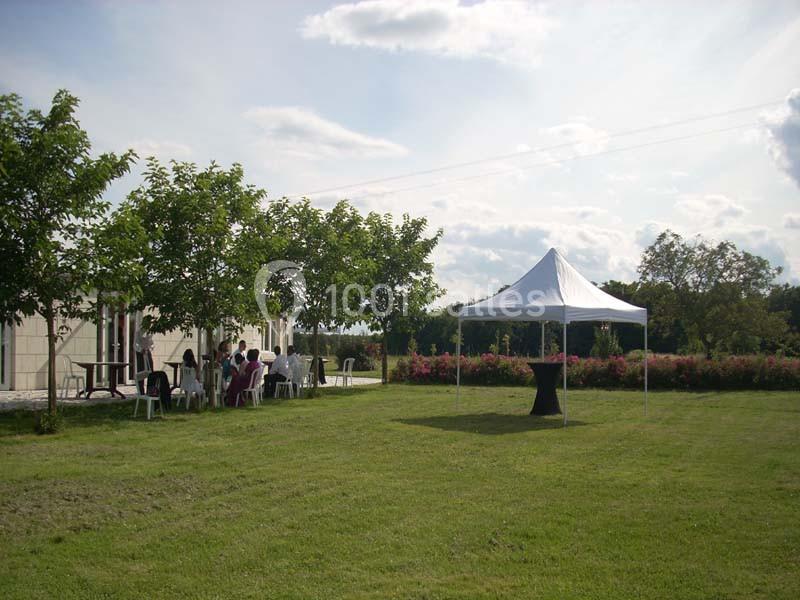 Un groupe de personnes assises sous des arbres près d'un bâtiment, avec une tente blanche sur une pelouse.