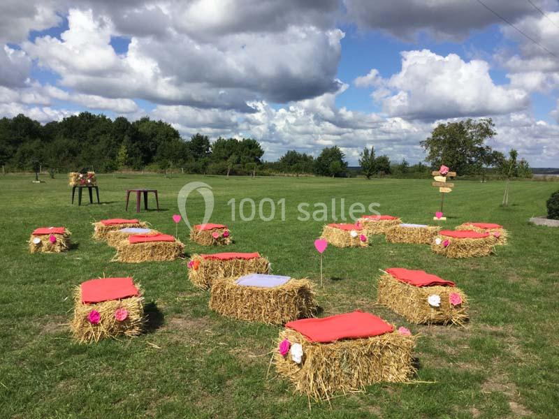 Bottes de paille décorées avec des coussins rouges disposées en extérieur sur une pelouse sous un ciel nuageux.