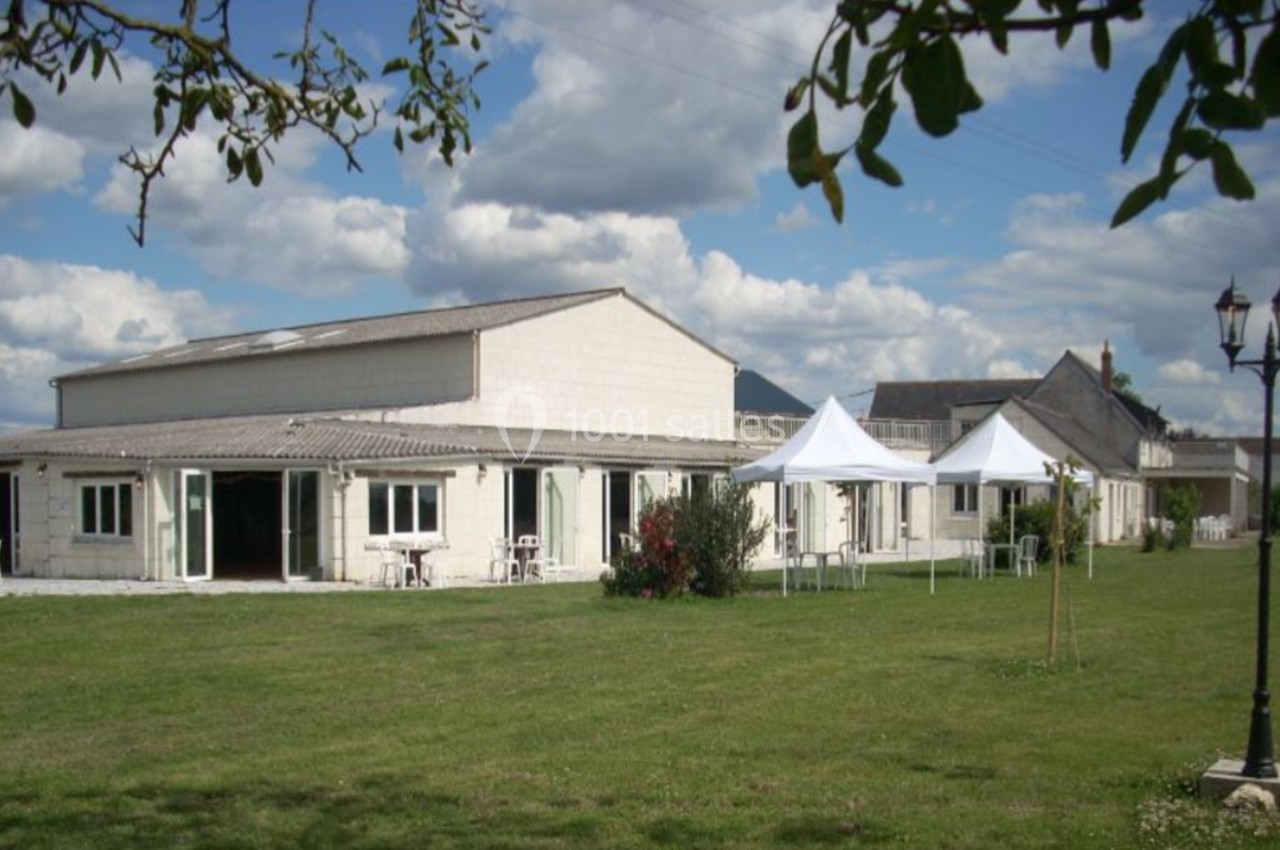Bâtiment clair avec grandes baies vitrées, pelouse au premier plan et tentes blanches installées à l'extérieur.