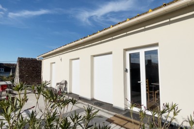 Chambre mansardée avec lit double, poutre apparente, télévision murale, commode, chaise et lampe de chevet.