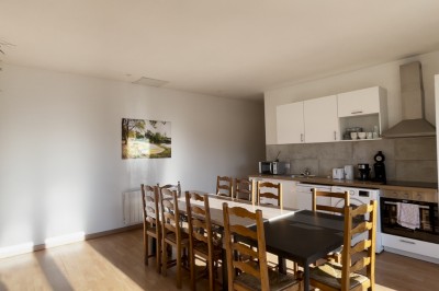 Chambre mansardée avec lit double, poutre apparente, télévision murale, commode, chaise et lampe de chevet.