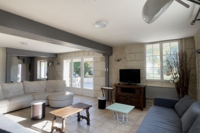 Chambre mansardée avec lit double, poutre apparente, télévision murale, commode, chaise et lampe de chevet.