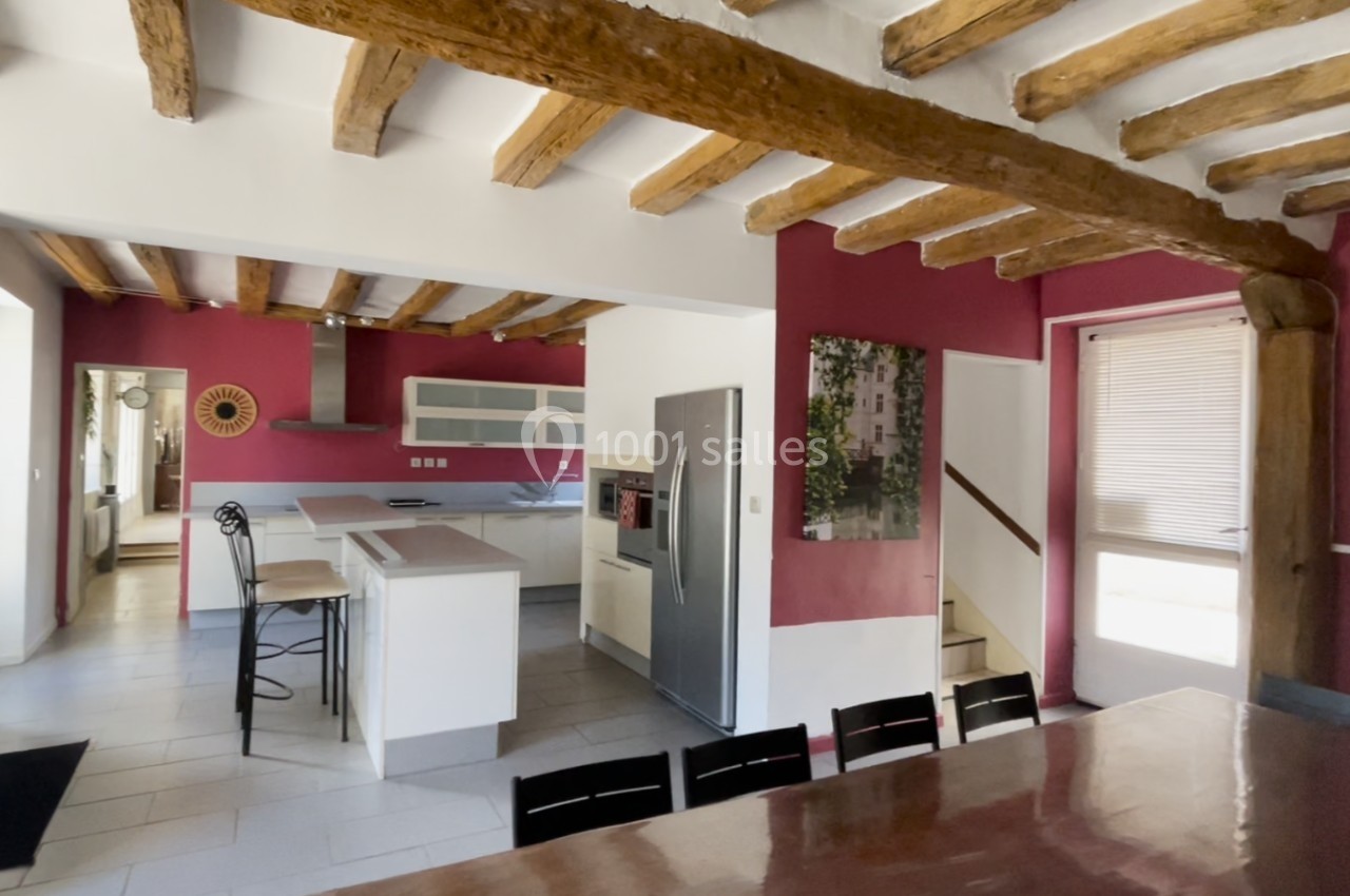 Cuisine ouverte avec poutres apparentes, murs rouges, îlot central, électroménagers modernes et lumière naturelle.