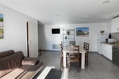 Chambre mansardée avec lit double, poutre apparente, télévision murale, commode, chaise et lampe de chevet.