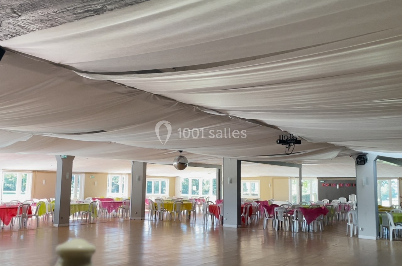 Salle de réception lumineuse avec plafond drapé, tables rondes dressées et chaises colorées.