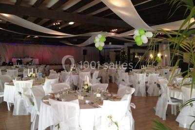 Chambre mansardée avec lit double, poutre apparente, télévision murale, commode, chaise et lampe de chevet.