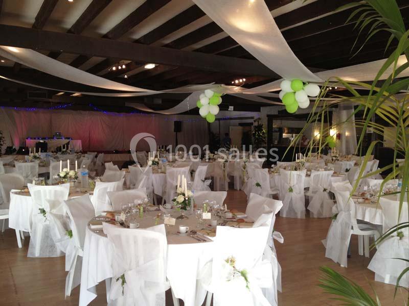 Salle de réception décorée avec des tables rondes, nappes blanches, chaises habillées et guirlandes suspendues.