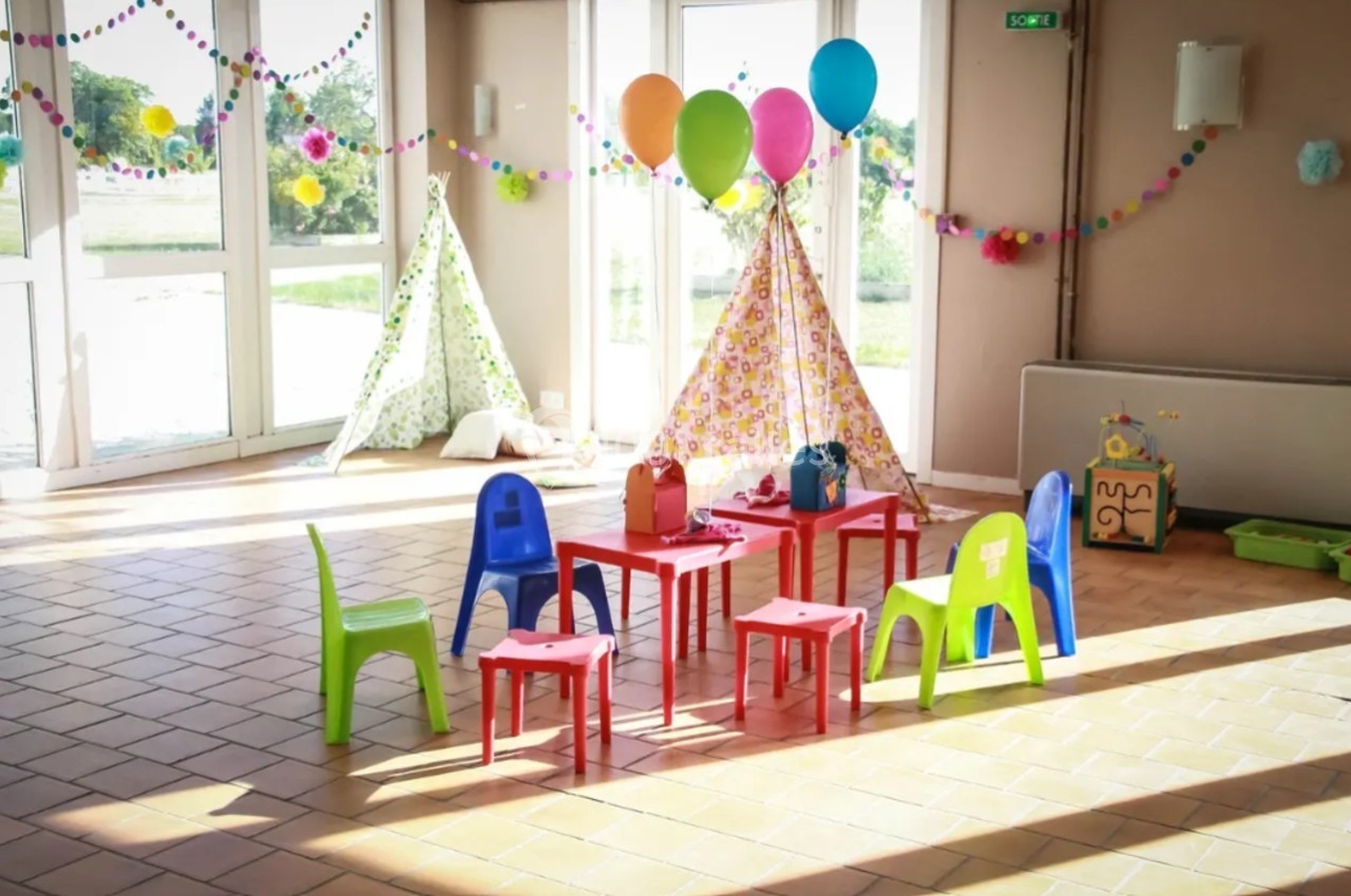 Salle décorée pour une fête d'enfants avec des tentes, des ballons colorés et des petites chaises autour de tables.