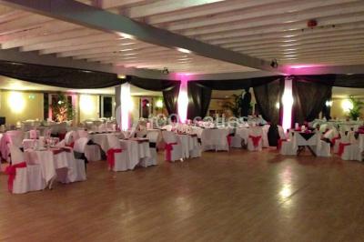 Chambre mansardée avec lit double, poutre apparente, télévision murale, commode, chaise et lampe de chevet.