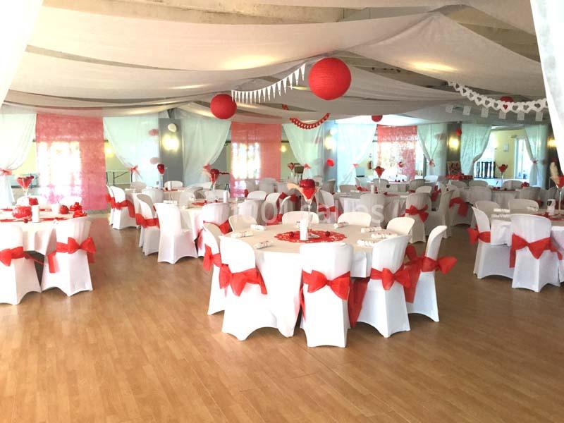 Salle de réception décorée avec des nappes blanches, des nœuds rouges et des lampions suspendus.
