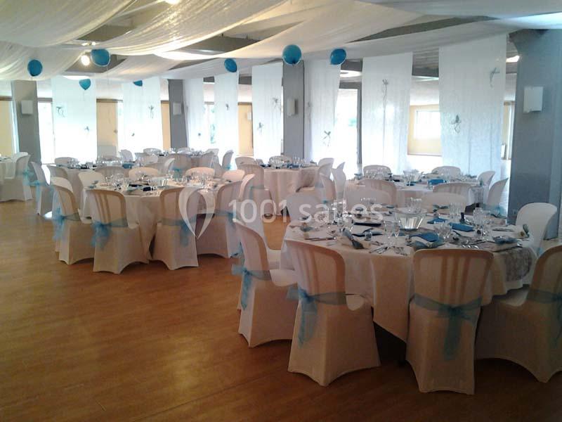 Salle de réception décorée avec des tables rondes, nappes blanches, chaises habillées et touches de bleu.