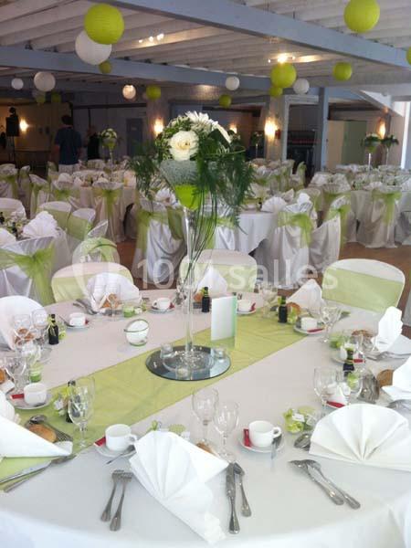 Salle de réception décorée pour un mariage, avec tables rondes dressées, nappes blanches et accents verts.