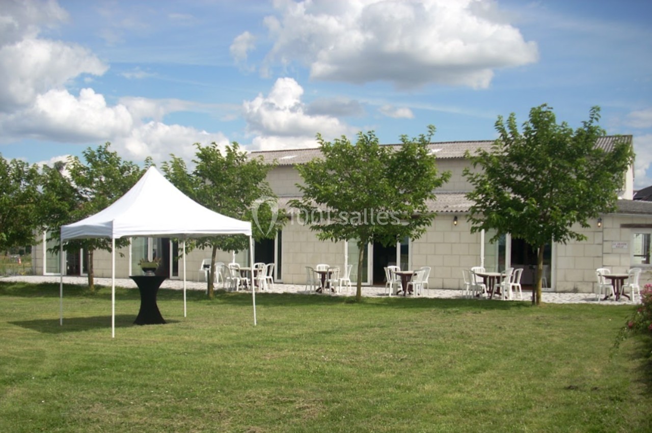 Tente blanche sur une pelouse devant un bâtiment en pierre avec des tables et des chaises disposées en extérieur.