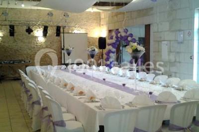 Chambre mansardée avec lit double, poutre apparente, télévision murale, commode, chaise et lampe de chevet.