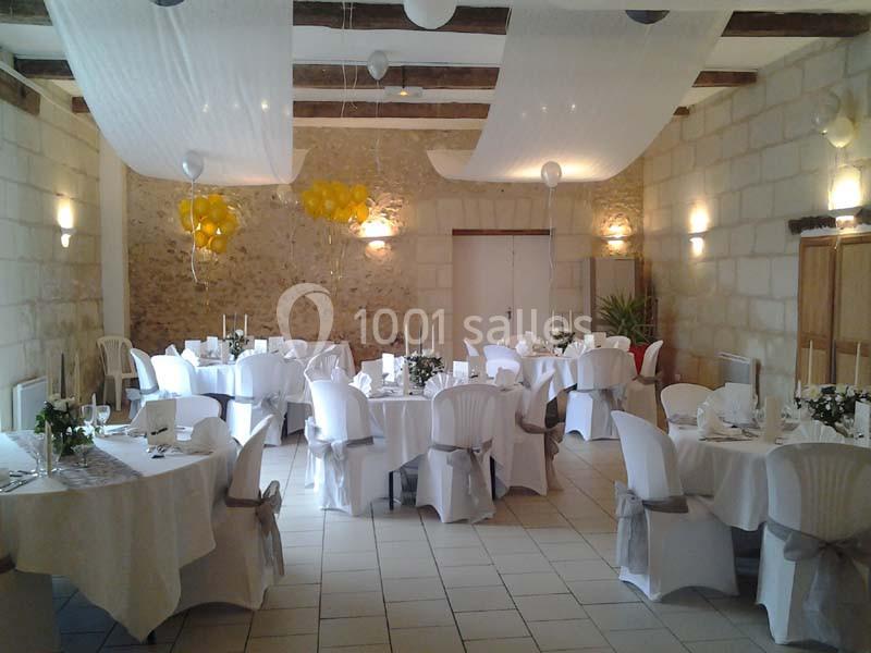 Salle de réception décorée avec des tables rondes, nappes blanches, chaises habillées et ballons jaunes.