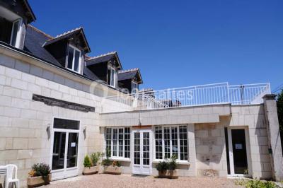 Chambre mansardée avec lit double, poutre apparente, télévision murale, commode, chaise et lampe de chevet.