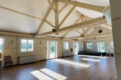 Chambre mansardée avec lit double, poutre apparente, télévision murale, commode, chaise et lampe de chevet.