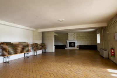 Chambre mansardée avec lit double, poutre apparente, télévision murale, commode, chaise et lampe de chevet.