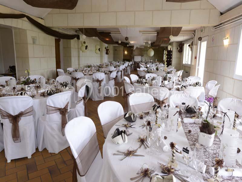 Salle de réception décorée avec des tables rondes, nappes blanches, chaises houssées et ornements marron.