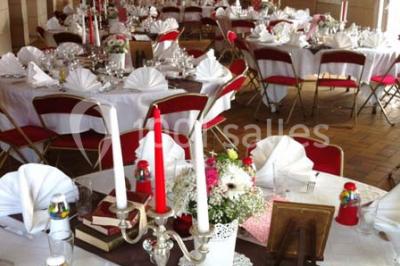 Chambre mansardée avec lit double, poutre apparente, télévision murale, commode, chaise et lampe de chevet.