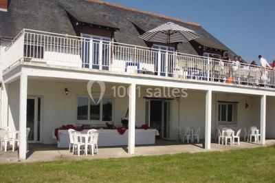 Chambre mansardée avec lit double, poutre apparente, télévision murale, commode, chaise et lampe de chevet.