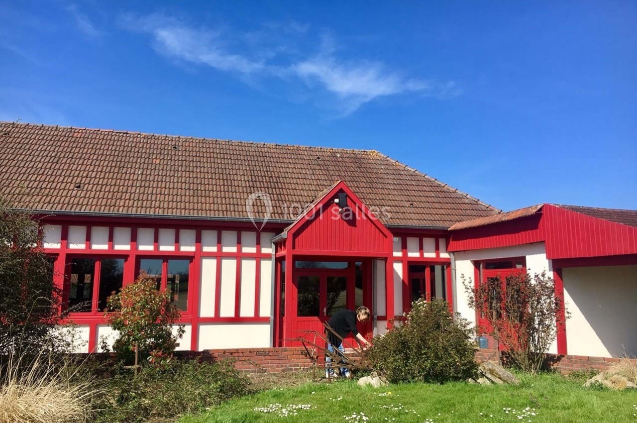 Façade d'une maison à colombages rouges et blancs avec un jardin verdoyant sous un ciel bleu.