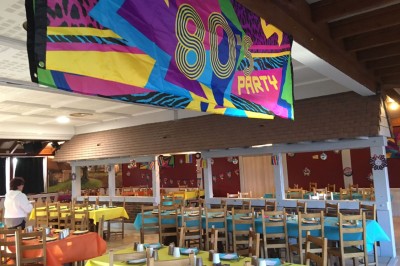 Salle décorée sur le thème des années 80 avec des invités assis à des tables lors d'un repas festif.