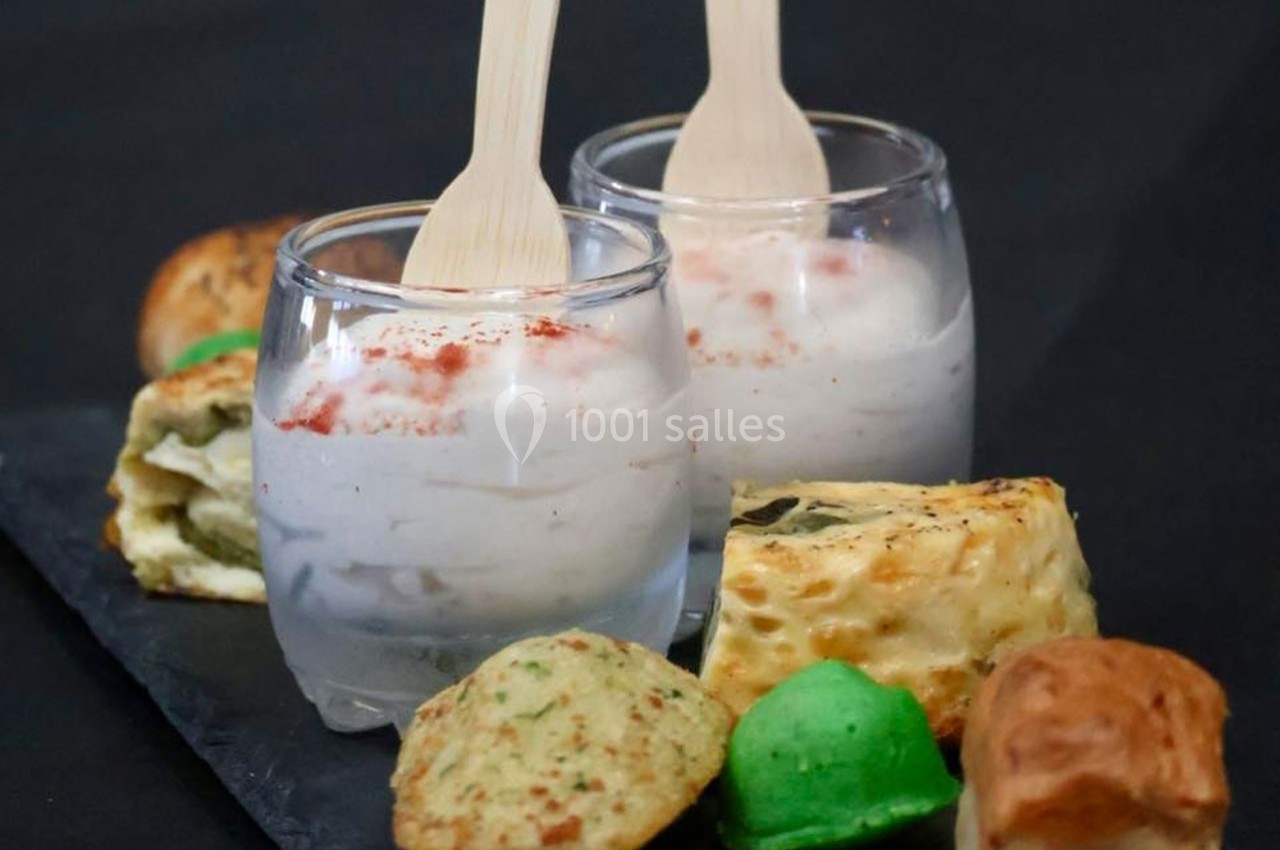 Deux verrines de soupe blanche garnies de paprika, accompagnées de petits pains variés sur une ardoise noire.