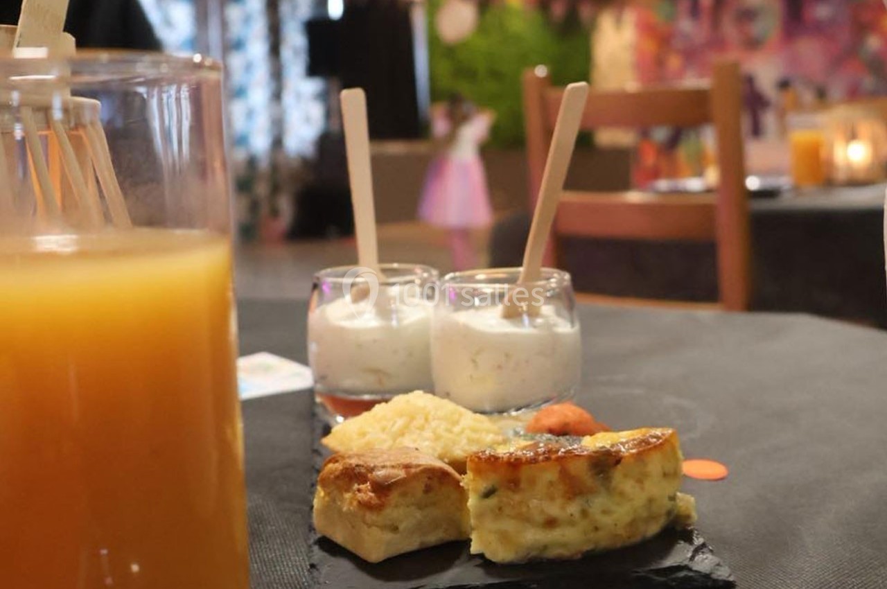 Assiette avec quiche, riz et verrines de dessert sur une table noire, avec un verre de jus d'orange au premier plan.