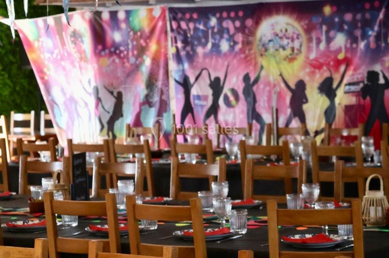 Salle décorée pour un événement festif, avec tables dressées et fond coloré représentant des silhouettes dansantes.