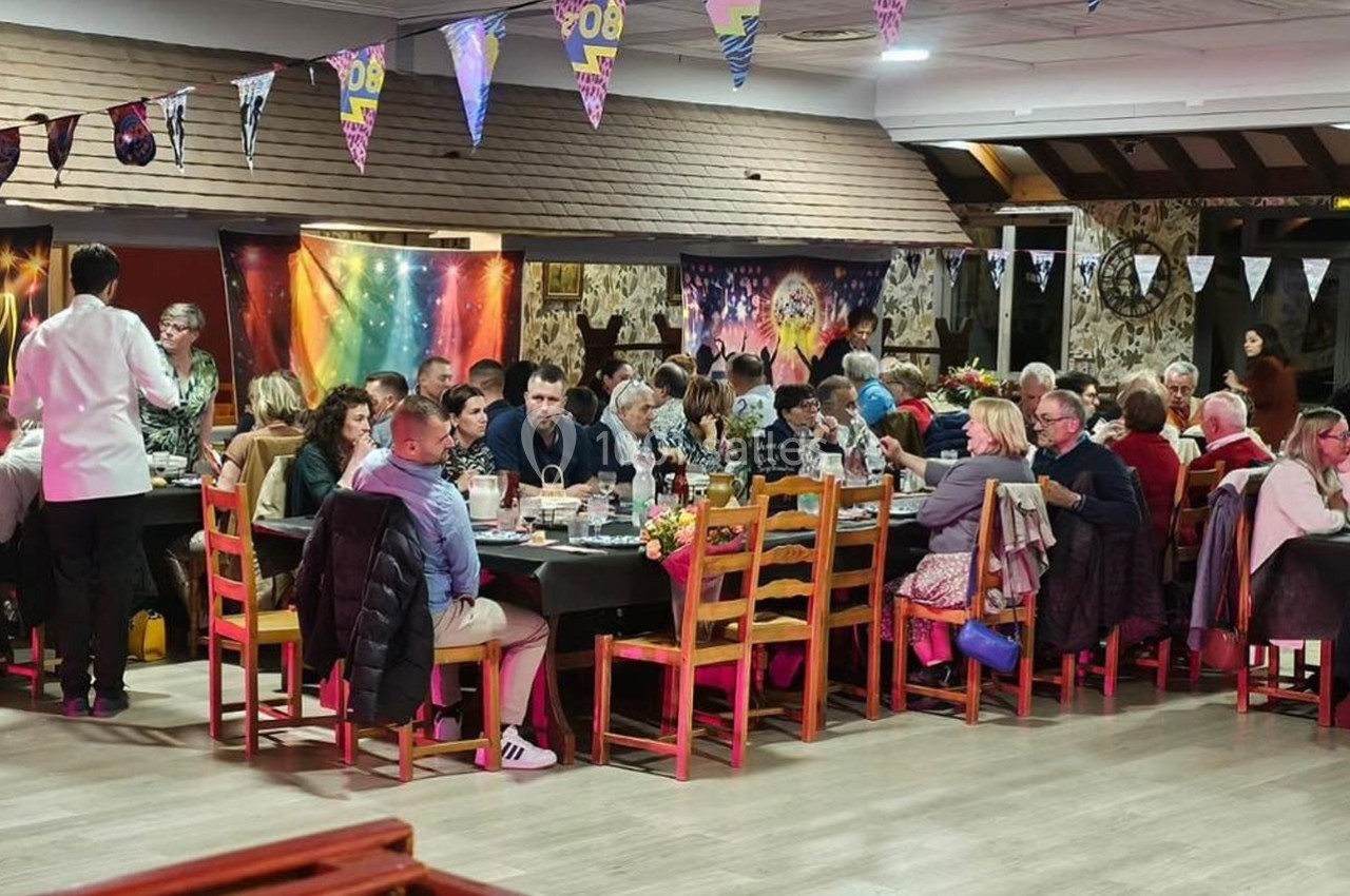 Des personnes assises autour de grandes tables dans une salle décorée, partageant un repas convivial.