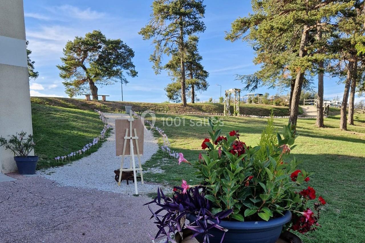 Chemin gravillonné bordé de fleurs menant à un chevalet en plein air, entouré d'arbres et de pelouse.