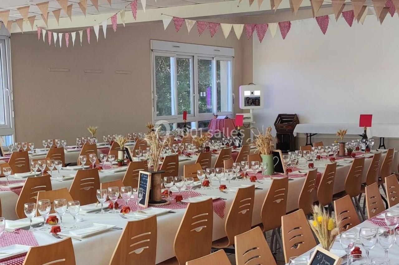 Salle décorée pour un repas festif avec tables dressées, nappes blanches, chemins de table rouges et guirlandes suspendues.
