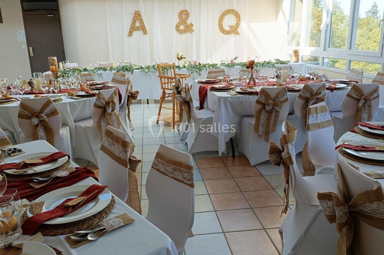 Salle de réception décorée pour un mariage, avec des tables dressées, des chaises ornées de rubans et des initiales ’A & Q…