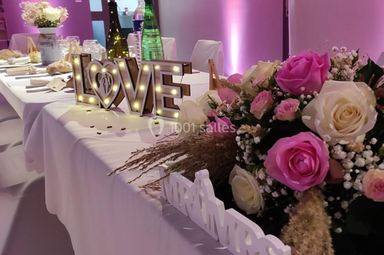 Table décorée pour un événement avec bouquet de roses, lettres lumineuses ’LOVE’ et bouteilles en arrière-plan.