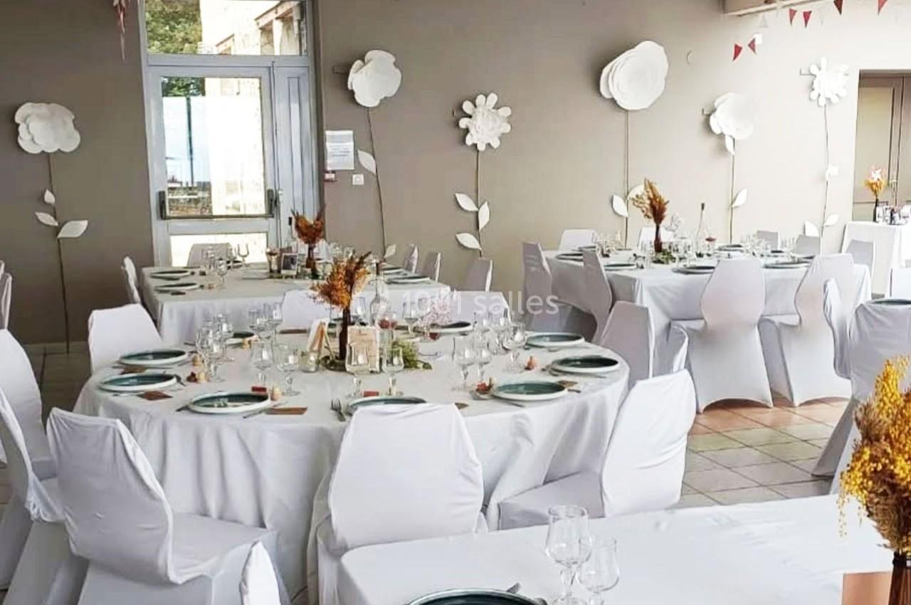 Salle de réception décorée avec des tables rondes dressées, nappes blanches et ornements floraux.