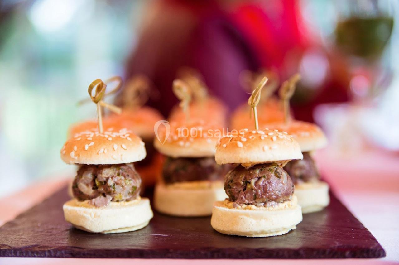 Mini-burgers surmontés de piques en bois, disposés sur une ardoise, avec un arrière-plan flou.