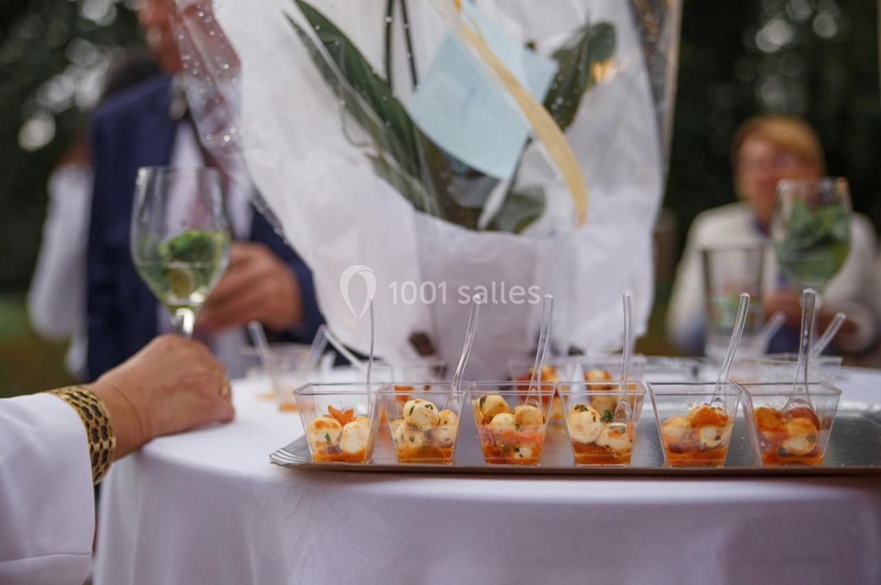 Plateau de verrines apéritives disposé sur une table blanche, entourée de convives avec des verres à la main.