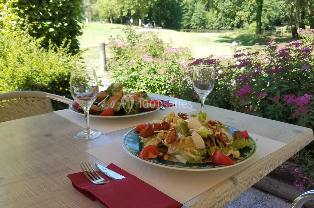 Deux assiettes de salade garnie avec couverts et verres, disposées sur une table en terrasse face à un jardin verdoyant.