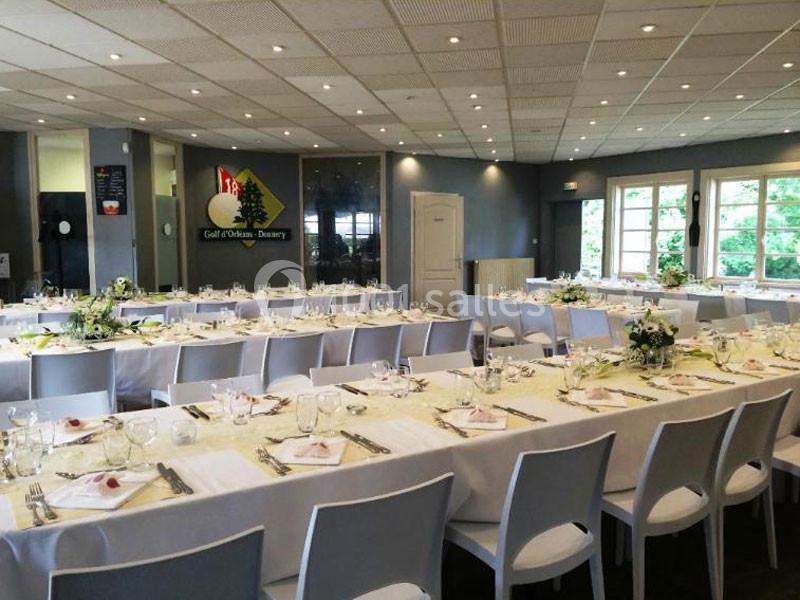 Salle de réception lumineuse avec tables dressées, nappes blanches, chaises modernes et décorations florales.