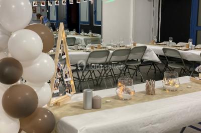 Salle décorée pour un événement avec des arches et colonnes de ballons beige et blanc, tables dressées avec vaisselle.