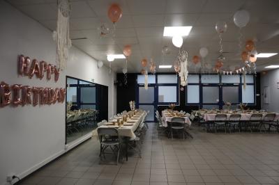 Salle décorée pour un événement avec des arches et colonnes de ballons beige et blanc, tables dressées avec vaisselle.