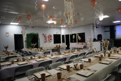 Salle décorée pour un événement avec des arches et colonnes de ballons beige et blanc, tables dressées avec vaisselle.