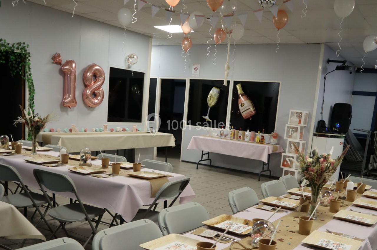 Salle décorée pour un 18e anniversaire avec tables dressées, ballons, guirlandes et arrangements floraux.