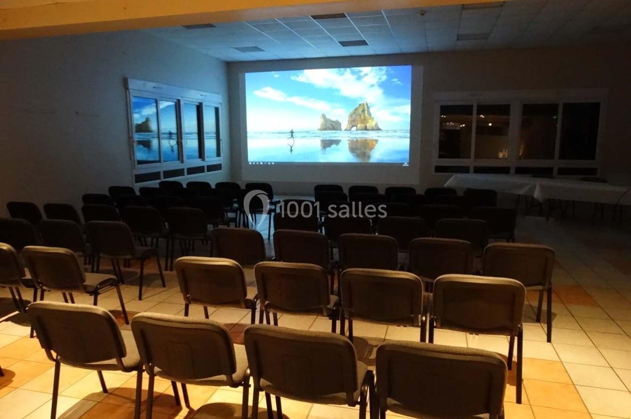 Salle équipée de chaises alignées face à un écran de projection affichant un paysage côtier.