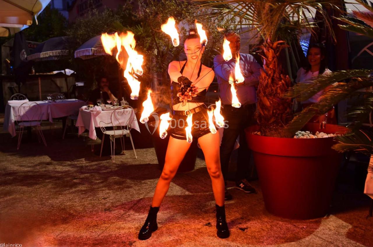 Une artiste jongle avec des torches enflammées dans un espace extérieur éclairé, entourée de spectateurs.