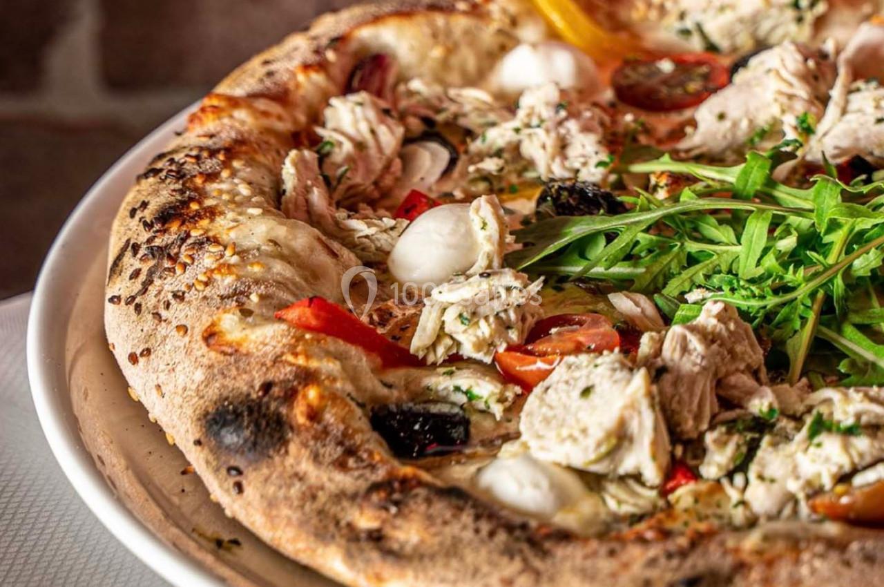 Pizza garnie de poulet, tomates cerises, mozzarella, roquette et herbes, servie sur une pâte dorée et croustillante.