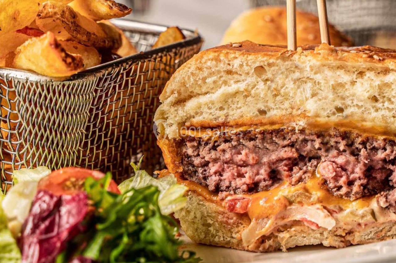 Burger coupé en deux montrant une viande juteuse, fromage fondu, légumes, accompagné de frites et salade.