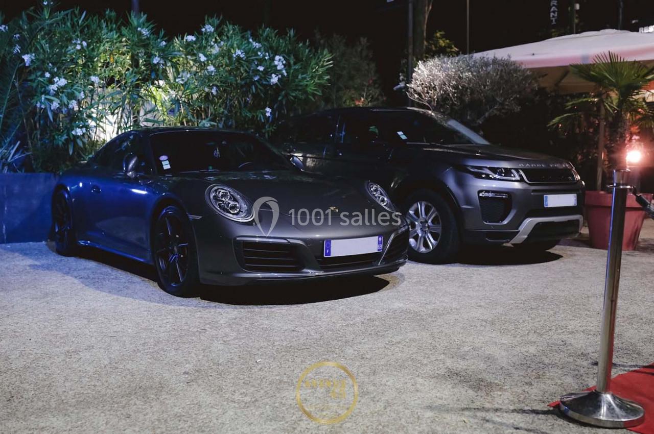 Deux voitures de luxe, une Porsche grise et un SUV noir, stationnées côte à côte dans un espace extérieur éclairé.